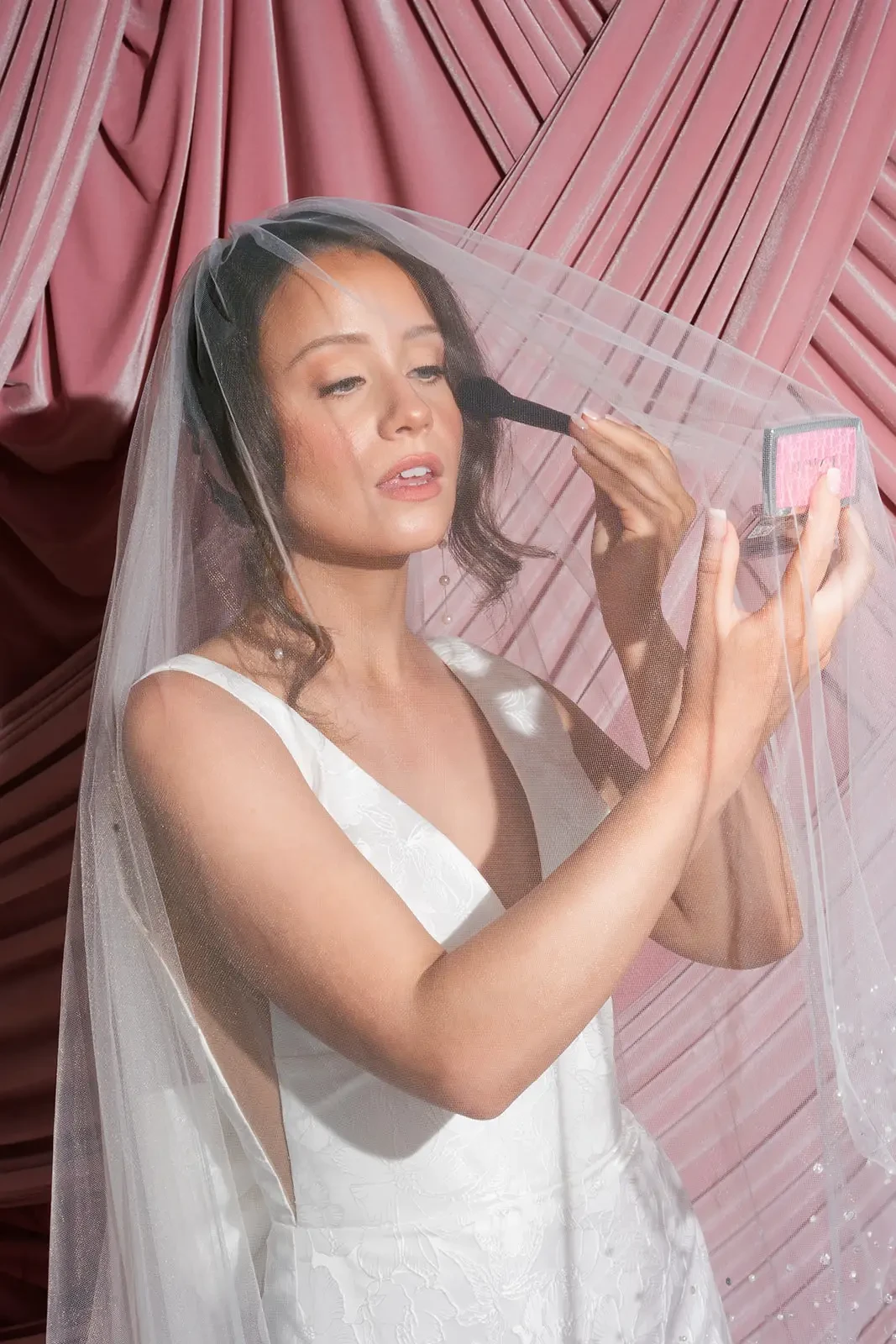 image shows a model touching up her makeup in a wedding dress and veil