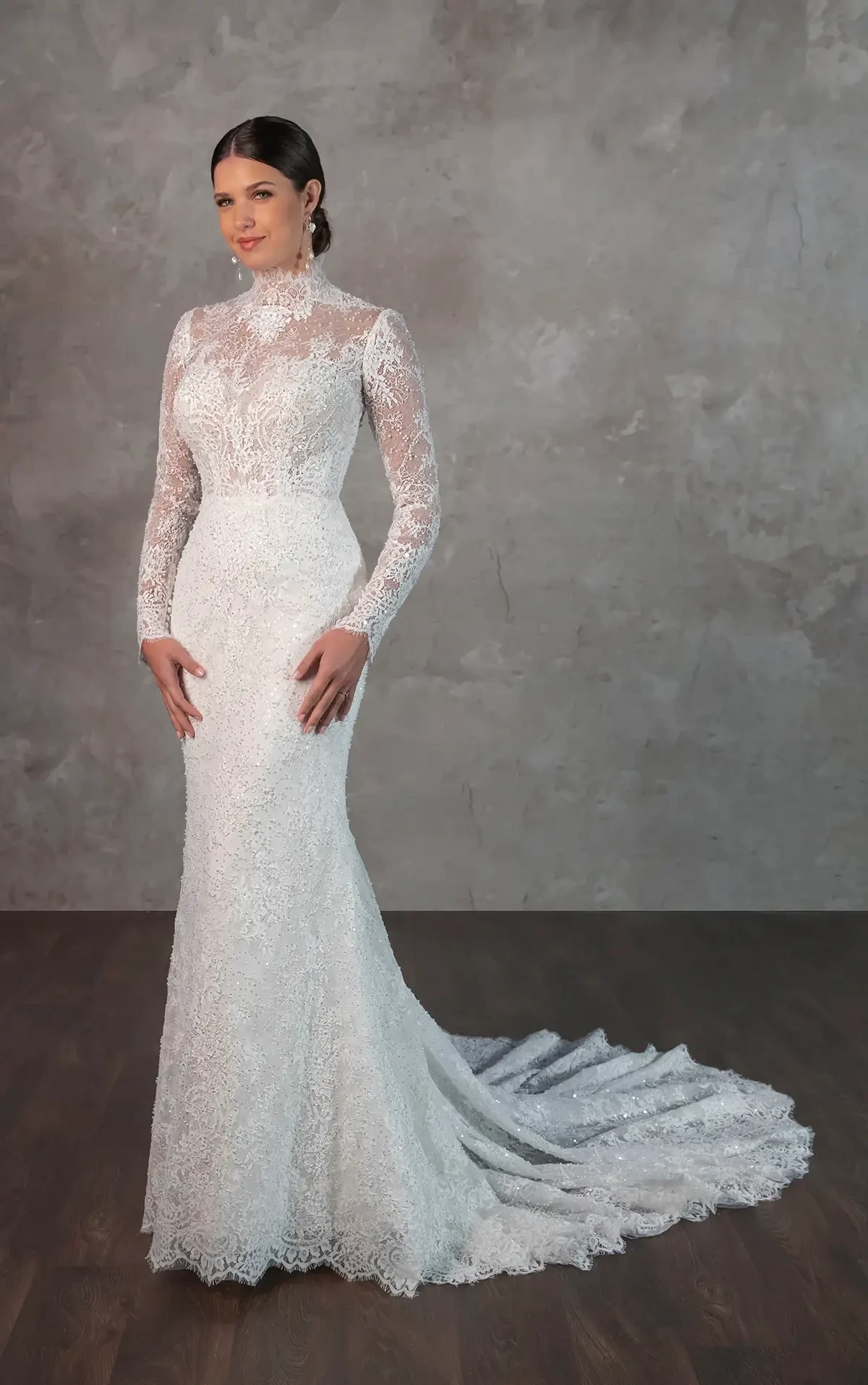 Model is wearing an Essense of Australia #D4294 gown, with a sheer all-lace bodice, delicate eyelash lace trim, fabric-covered buttons down the spine, and a column sheath silhouette with a sweeping train.
