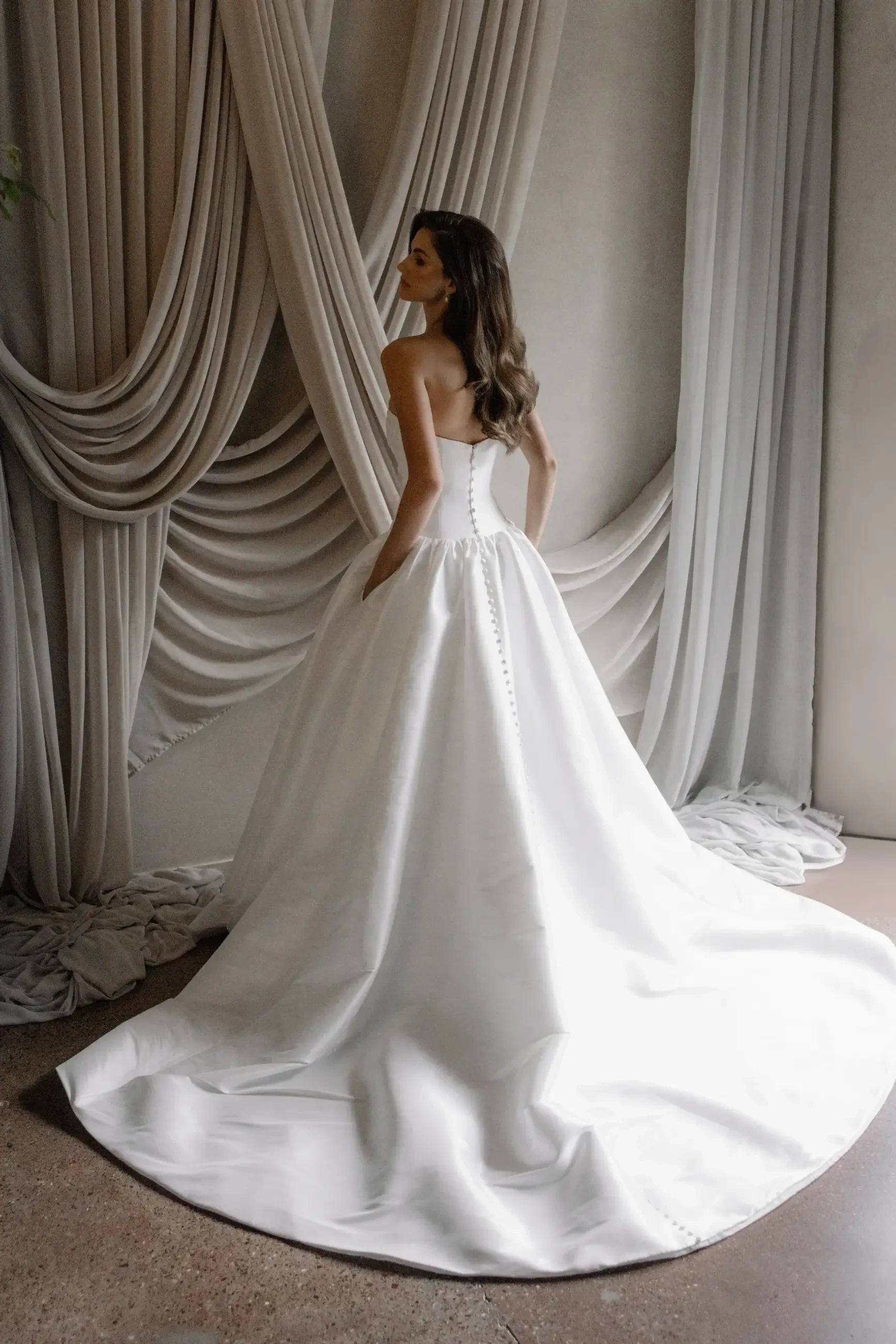 Model is wearing a Trish Peng #Aneta gown, with a modern drop waist, luxurious stretch Mikado fabric, expert ruching through the bodice, and a flowing A-line skirt.