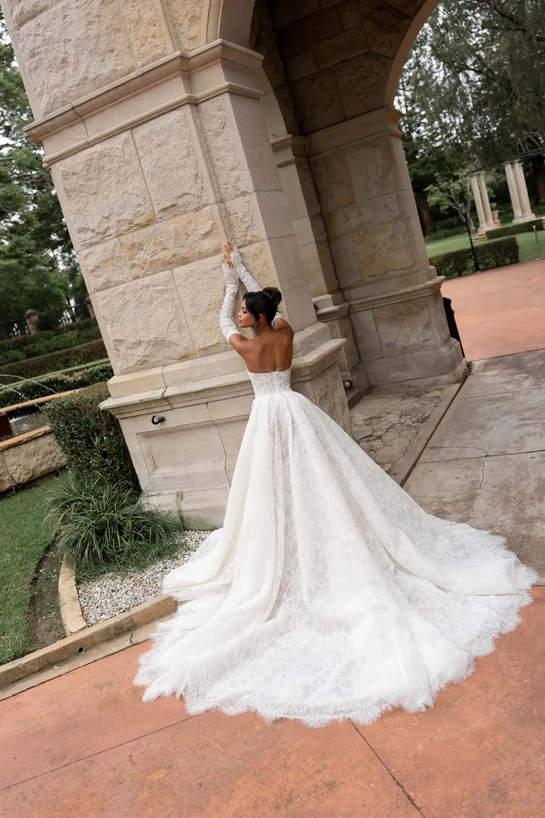 Model is wearing the Harper gown by Lé Lee Studio, an A-line chantilly lace dress with diagonal boning corsetry, semi-transparent lace detailing, and fully detachable sleeves and veil.