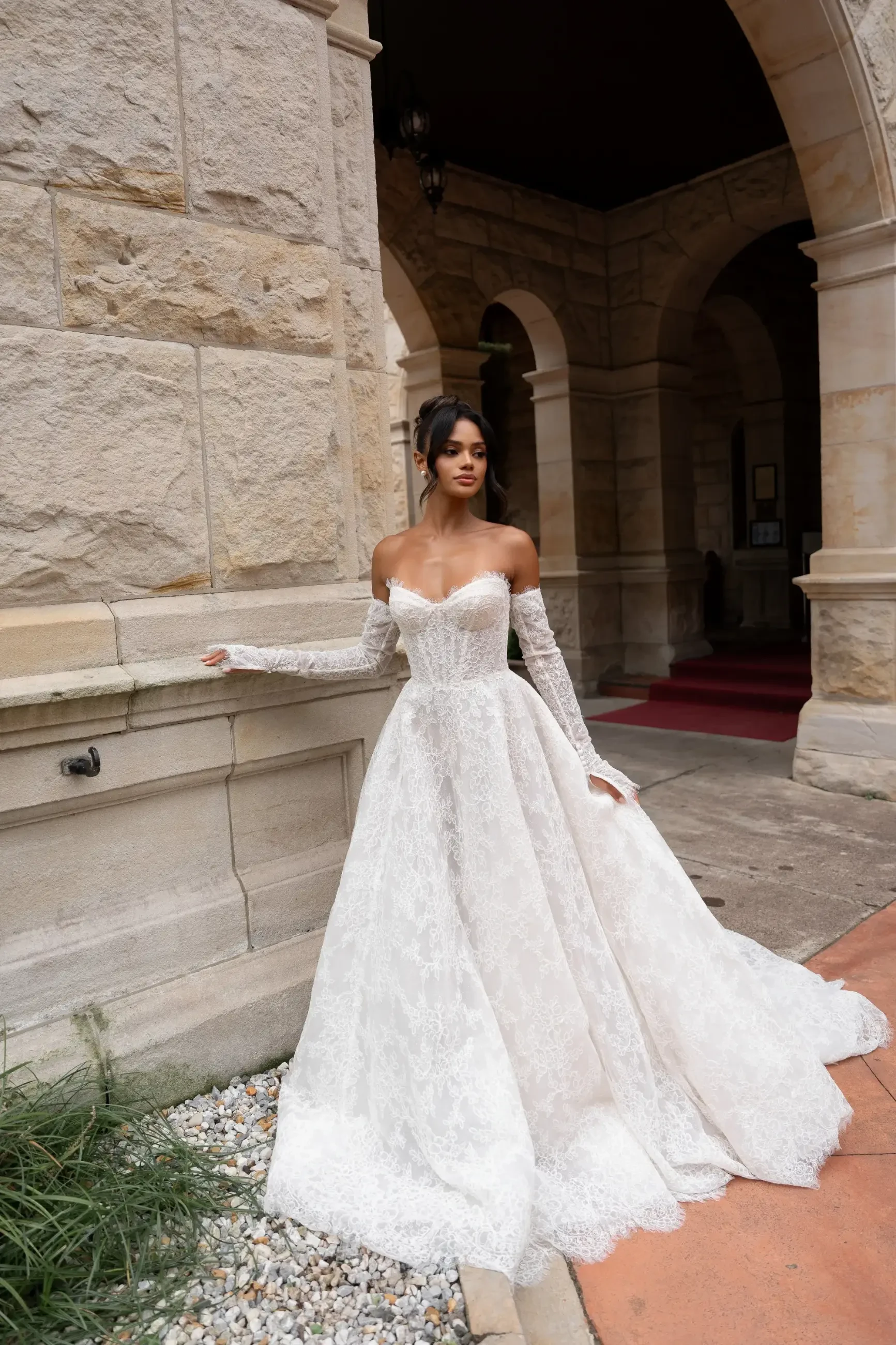 Model is wearing the Harper gown by Lé Lee Studio, an A-line chantilly lace dress with diagonal boning corsetry, semi-transparent lace detailing, and fully detachable sleeves and veil.