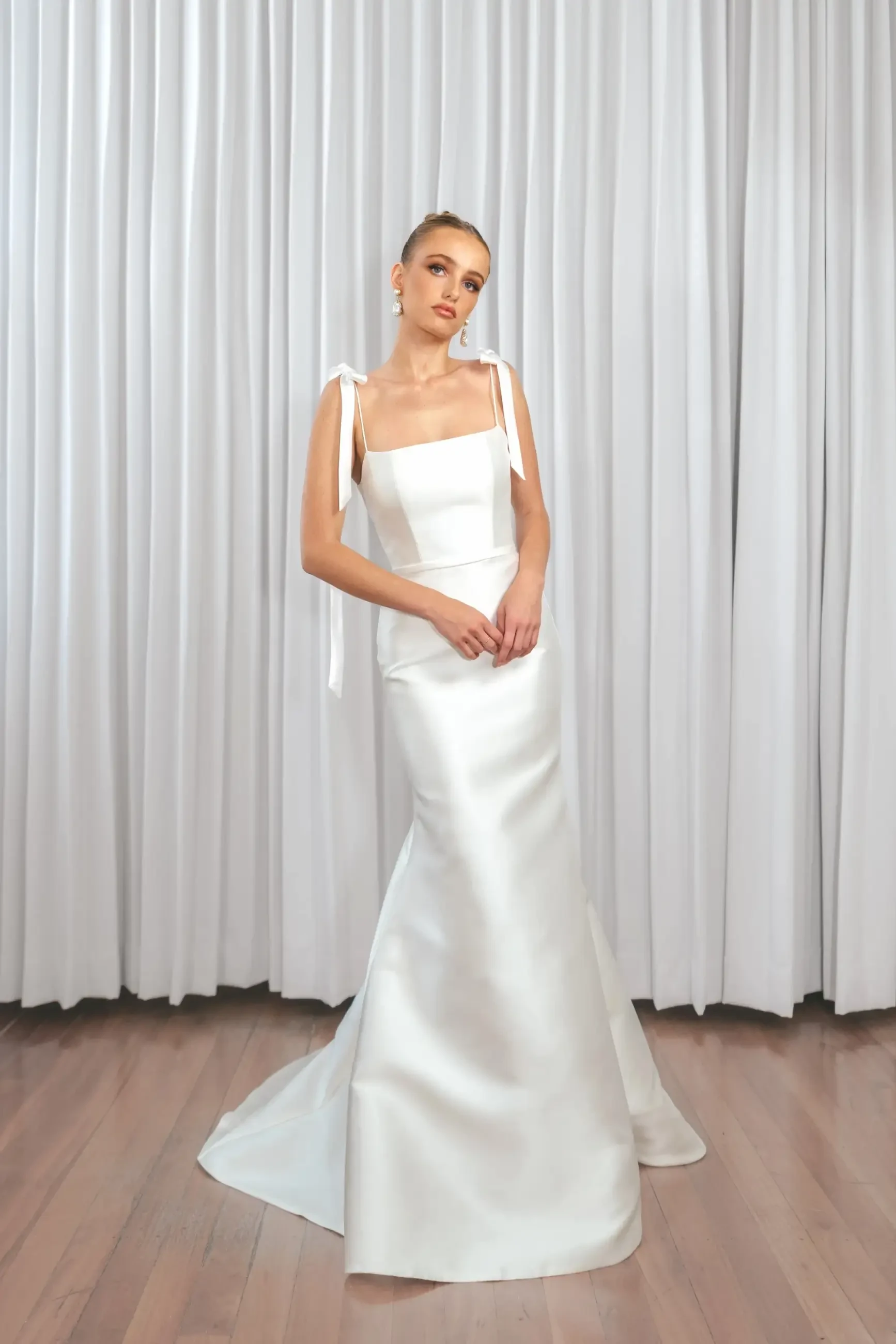 Model is wearing a Mikado fit-and-flare wedding gown with a square neckline and barely-there straps for a structured yet refined bridal look.