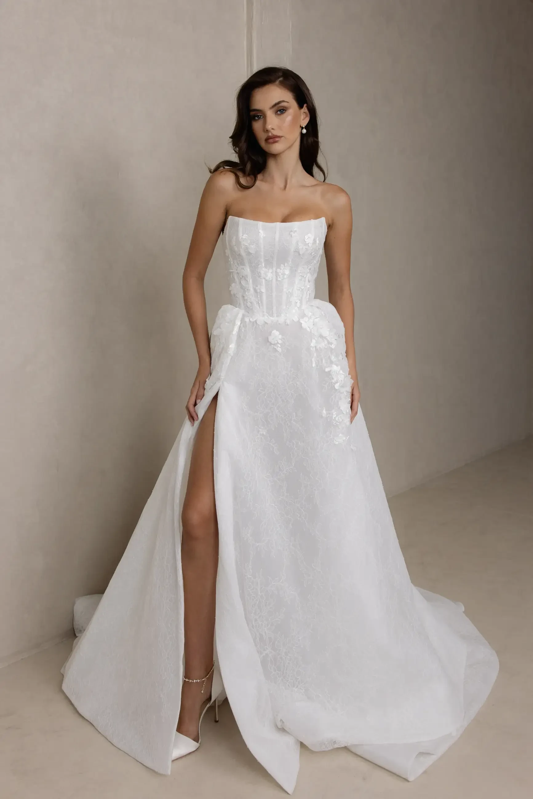 Model is wearing a soft A-line gown with a scoop neckline, structured lace bodice, and 3D floral appliqués throughout the skirt.